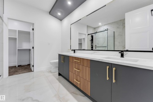 Spacious bathroom featuring a dual vanity with a white countertop and integrated sinks, matte black faucets, and gold-tone hardware - 131 24 Street, Edmonton, AB 