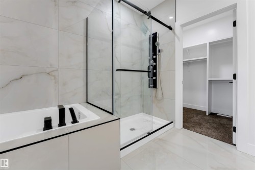 Bathroom featuring a built-in soaking tub with matte black fixtures, a walk-in shower with a glass enclosure and multi-function shower panel, and large format white tile flooring and wall surrounds - 131 24 Street, Edmonton, AB 