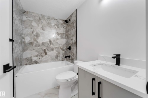 Contemporary bathroom featuring a white tub, large format marble-look wall tiles, and matte black fixtures - 131 24 Street, Edmonton, AB 