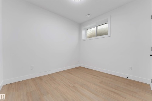 Room featuring light wood-finish flooring, white painted walls, and a single window with privacy glass - 131 24 Street, Edmonton, AB 