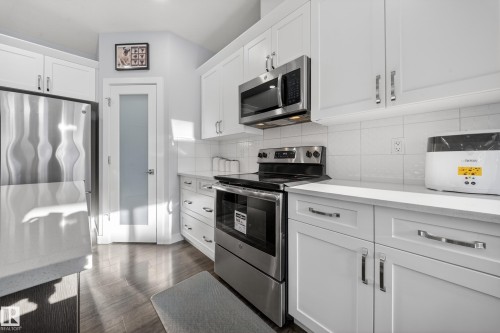 Modern kitchen featuring white cabinetry, stainless steel appliances, light countertops, and wood-finish flooring - 2084 Graydon Hill, Edmonton, AB 