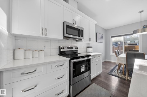 Contemporary kitchen featuring white cabinetry with brushed chrome hardware, a white tile backsplash, and light-colored countertops - 2084 Graydon Hill, Edmonton, AB 