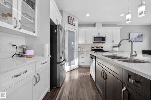 Modern kitchen featuring white shaker cabinetry, stainless steel appliances, a center island with a double basin sink, light-toned countertops, and wood-finish flooring - 2084 Graydon Hill, Edmonton, AB 