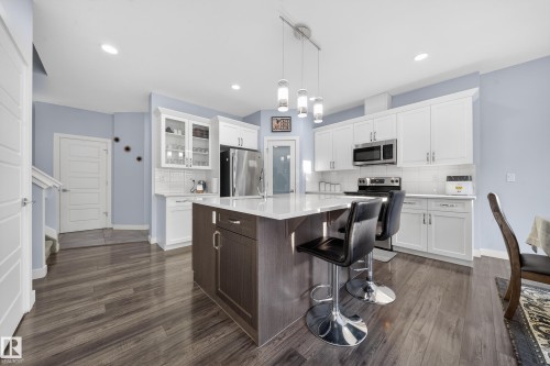 Open-concept kitchen featuring an island with counter seating, a white subway tile backsplash, stainless steel appliances, and wood-finish flooring - 2084 Graydon Hill, Edmonton, AB 