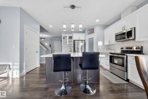 Contemporary kitchen featuring a central island with countertop seating, stainless steel appliances, white cabinetry, and wood-finish flooring - 2084 Graydon Hill, Edmonton, AB 