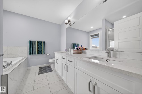 Bathroom featuring a dual vanity with white cabinetry and light-colored countertops, a built-in bathtub with tile surround, a built-in shower with glass enclosure, and light-colored tile flooring - 2084 Graydon Hill, Edmonton, AB 