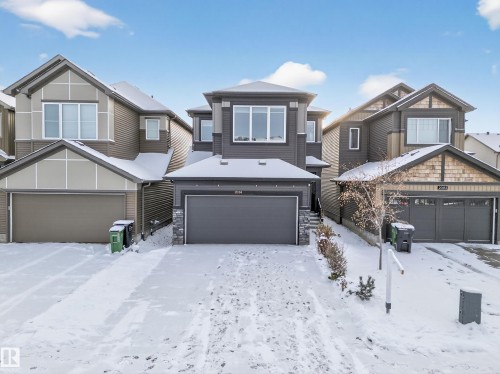 Contemporary two-story residence featuring a dark gray facade with stone accents, a double-car garage, and multiple windows - 2084 Graydon Hill, Edmonton, AB 