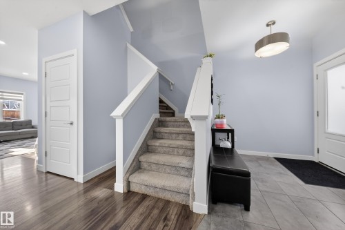 Inviting entryway featuring a carpeted staircase with white railings, wood-finish flooring, and light-toned wall paint - 2084 Graydon Hill, Edmonton, AB 