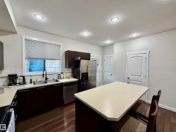 Kitchen featuring dark wood-finish cabinetry, stainless steel appliances, a double basin sink with a gooseneck faucet, light-toned countertops, and recessed lighting - 