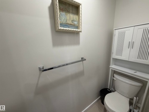 Bathroom featuring a white toilet, chrome towel bar, and white wall-mounted storage cabinet with slatted doors - 45 6075 Schonsee Way, Edmonton, AB 