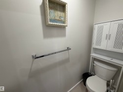 Bathroom featuring a white toilet, chrome towel bar, and white wall-mounted storage cabinet with slatted doors - 