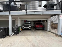 Two-car garage with overhead lighting, featuring a concrete driveway and an upper-level balcony with black railings - 