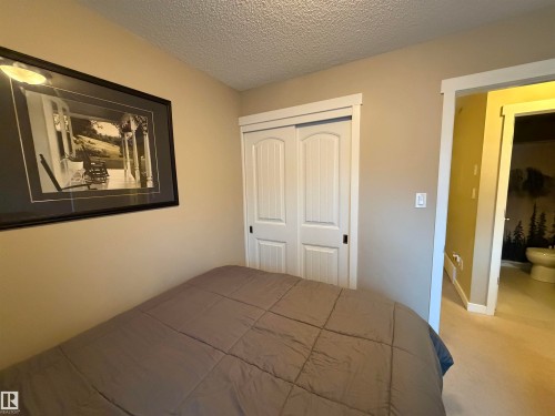 Neutral-toned room featuring a textured ceiling, a built-in closet with white panel doors, and a doorway to a separate space with a toilet - 45 6075 Schonsee Way, Edmonton, AB 