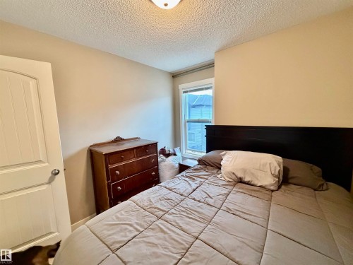 Neutral-toned bedroom featuring a single window with white trim, a wood-finish door, and textured ceiling - 45 6075 Schonsee Way, Edmonton, AB 