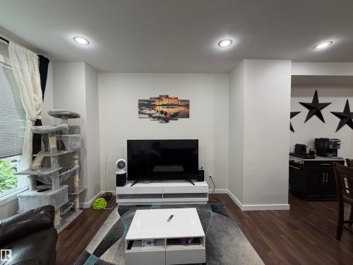 Recessed ceiling lighting illuminates a living area featuring wood-finish flooring and white baseboards - 45 6075 Schonsee Way, Edmonton, AB 