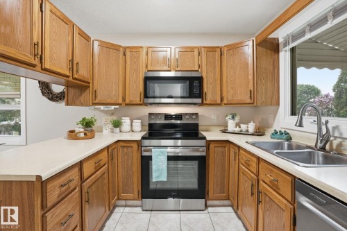 U-shaped kitchen featuring wood cabinetry, light countertops, and stainless steel appliances, including an oven/range, microwave, and dishwasher - 1008 61 Street, Edmonton, AB 