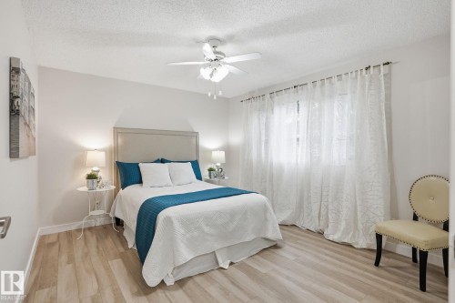 Spacious room featuring wood-finish flooring, a white ceiling fan, and large windows with privacy sheers - 1008 61 Street, Edmonton, AB 