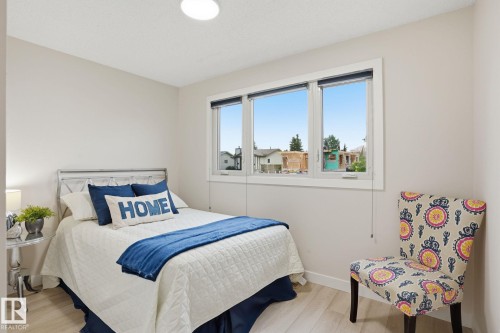 Light-filled room featuring a large window, light wood-finish flooring, white baseboards, and a flush-mount ceiling light - 1008 61 Street, Edmonton, AB 