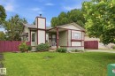 Exterior featuring light green stucco with burgundy trim, a front lawn, a burgundy privacy fence, a covered entry, and mature trees - 1008 61 Street, Edmonton, AB 
