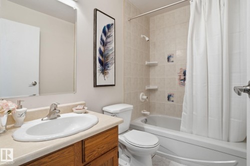 Bathroom featuring a full-size tub with shower, tiled surround, and a light wood-finish vanity with an integrated sink - 1008 61 Street, Edmonton, AB 
