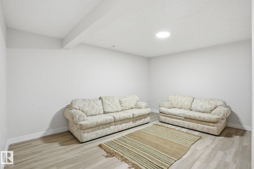 Spacious room featuring light-toned wood-finish flooring, white baseboards, and neutral wall tones - 1008 61 Street, Edmonton, AB 