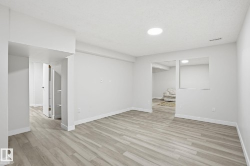 Spacious room featuring light wood-finish flooring, recessed lighting, neutral paint, and white baseboards - 1008 61 Street, Edmonton, AB 