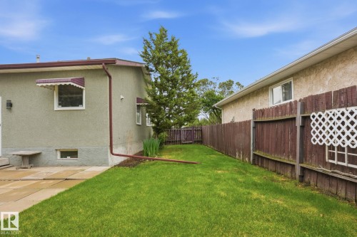 Expansive backyard featuring a manicured lawn, a full-height privacy fence, and a mature evergreen tree - 1008 61 Street, Edmonton, AB 