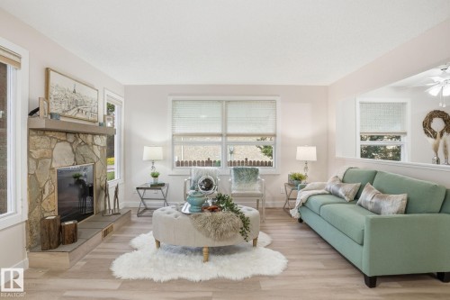 Living area featuring a stone-clad fireplace with a hearth, light wood-finish flooring, multiple windows, and a partial wall opening to an adjacent space - 1008 61 Street, Edmonton, AB 