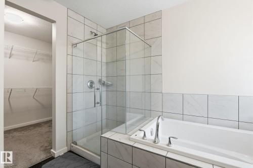 Shower with glass enclosure and light-toned tile surround, freestanding tub with chrome fixtures, and an adjacent walk-in closet with wire shelving - 20011 26, Edmonton, AB 