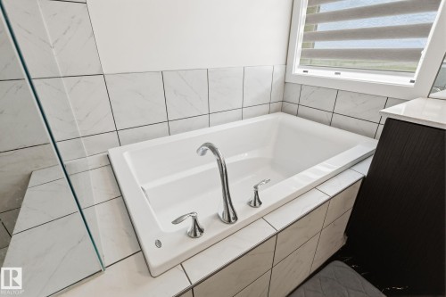 Built-in soaking tub with chrome fixtures, surrounded by white rectangular wall tiles - 20011 26, Edmonton, AB 