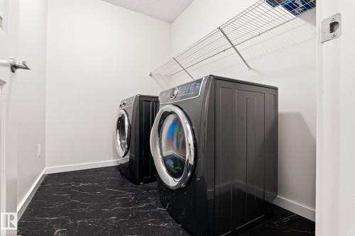 Dedicated laundry space featuring a dark finish washer and dryer, black marble-look flooring, white baseboards, and overhead wire shelving - 20011 26, Edmonton, AB 