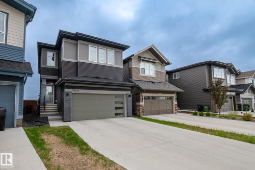 Contemporary exterior with mixed material facade, featuring a two-car garage with frosted glass inserts, concrete driveway, and a front entry with dark grey brick accents - 20011 26, Edmonton, AB 