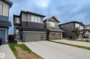 Contemporary exterior with mixed material facade, featuring a two-car garage with frosted glass inserts, concrete driveway, and a front entry with dark grey brick accents - 20011 26, Edmonton, AB 