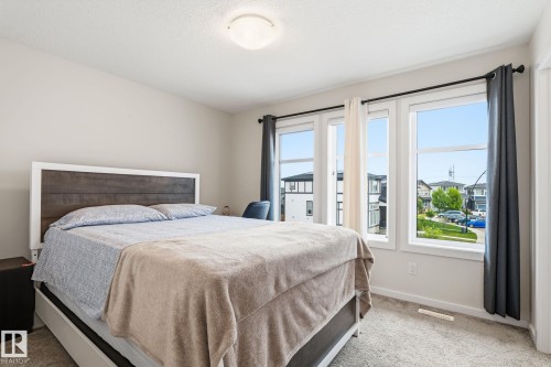 Bedroom featuring light neutral wall paint, carpeted flooring, and a multi-pane window with dark curtain rods - 20011 26, Edmonton, AB 