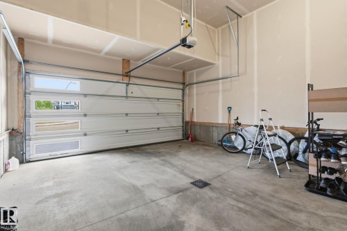 Spacious garage featuring a sectional overhead door with upper and middle rectangular window inserts, a concrete floor, and an automatic garage door opener - 20011 26, Edmonton, AB 