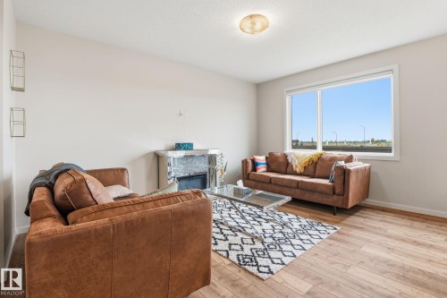 Living area featuring wood-finish flooring, a large window, a ceiling-mounted light fixture, and light-colored walls - 20011 26, Edmonton, AB 