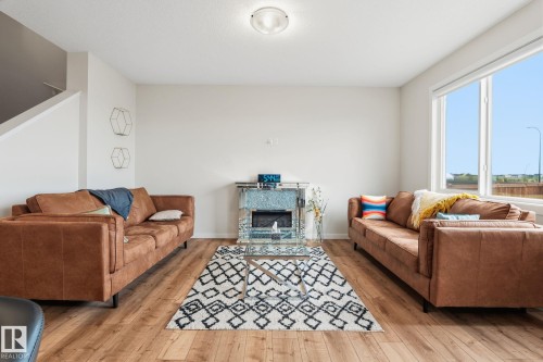 Bright living space featuring wood-finish flooring, a contemporary accent fireplace, and a white ceiling with a flush-mount light fixture - 20011 26, Edmonton, AB 