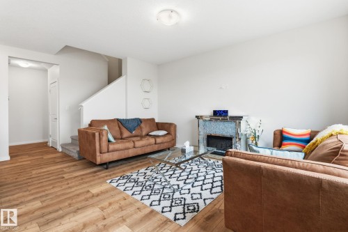 Spacious living area featuring wood-finish flooring, a contemporary mirrored fireplace surround, and a carpeted staircase - 20011 26, Edmonton, AB 