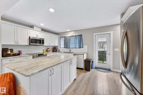 Kitchen featuring a central island with a stone countertop, white shaker cabinetry, stainless steel appliances, and wood-finish flooring - 85 165 Cy Becker Boulevard, Edmonton, AB - Indoor Photo Showing Kitchen With Upgraded Kitchen
