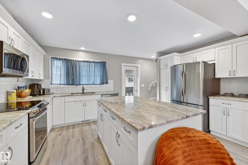 Contemporary kitchen featuring a substantial island with a stone-finish countertop, white cabinetry, and stainless steel appliances - 85 165 Cy Becker Boulevard, Edmonton, AB - Indoor Photo Showing Kitchen With Upgraded Kitchen