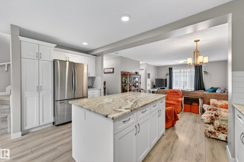 Kitchen featuring a central island with a stone countertop, white cabinetry, stainless steel refrigerator, and wood-finish flooring - 85 165 Cy Becker Boulevard, Edmonton, AB - Indoor Photo Showing Kitchen With Upgraded Kitchen
