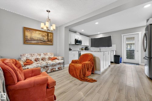Open-concept living space featuring wood-finish flooring, a contemporary chandelier, white kitchen cabinetry, a stainless steel refrigerator, and recessed lighting - 85 165 Cy Becker Boulevard, Edmonton, AB - Indoor Photo Showing Living Room