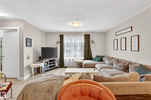 Living area featuring light gray wall paint, wood-finish flooring, and a large window with sheer and dark curtains - 85 165 Cy Becker Boulevard, Edmonton, AB - Indoor Photo Showing Living Room