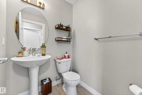 Powder room featuring a pedestal sink, oval mirror, and light wood-finish flooring - 85 165 Cy Becker Boulevard, Edmonton, AB - Indoor Photo Showing Bathroom