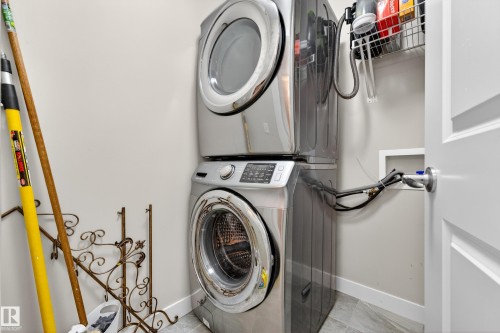 Dedicated laundry area featuring stacked front-load appliances, a wall-mounted wire shelf, and light gray wall paint - 85 165 Cy Becker Boulevard, Edmonton, AB - Indoor Photo Showing Laundry Room