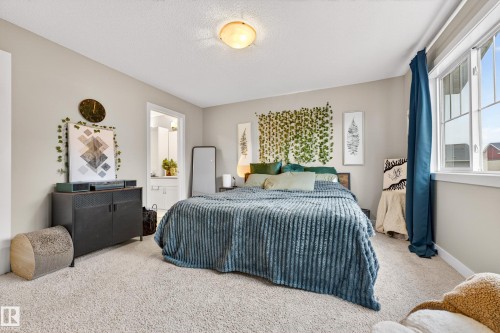 Carpeted room featuring a ceiling-mounted light fixture, an exposed window with a white frame, and a door leading to a bathroom with a vanity - 85 165 Cy Becker Boulevard, Edmonton, AB - Indoor Photo Showing Bedroom