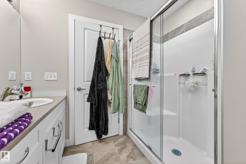 Bathroom featuring a glass-enclosed shower with a built-in bench, white vanity with an undermount sink, neutral countertop, and light-toned floor tiling - 85 165 Cy Becker Boulevard, Edmonton, AB - Indoor Photo Showing Bathroom