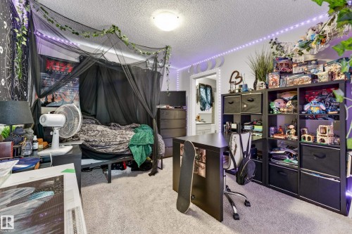 Carpeted bedroom featuring a bed with a black canopy, a built-in shelf system, a desk area, and a ceiling light fixture - 85 165 Cy Becker Boulevard, Edmonton, AB - Indoor