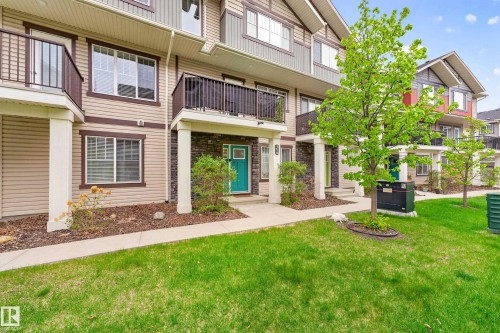 Multi-level townhouse exterior featuring beige siding with dark trim accents, a vibrant teal entry door, a ground-level patio, and an upper-level balcony with dark railings - 85 165 Cy Becker Boulevard, Edmonton, AB - Outdoor