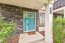 Entryway featuring a vibrant teal front door with transom windows, dark stacked stone facade, and a concrete landing - 85 165 Cy Becker Boulevard, Edmonton, AB  - Outdoor 